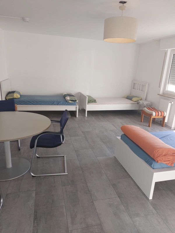 Mehrbettzimmer mit drei Betten, Rundtisch und Stühlen